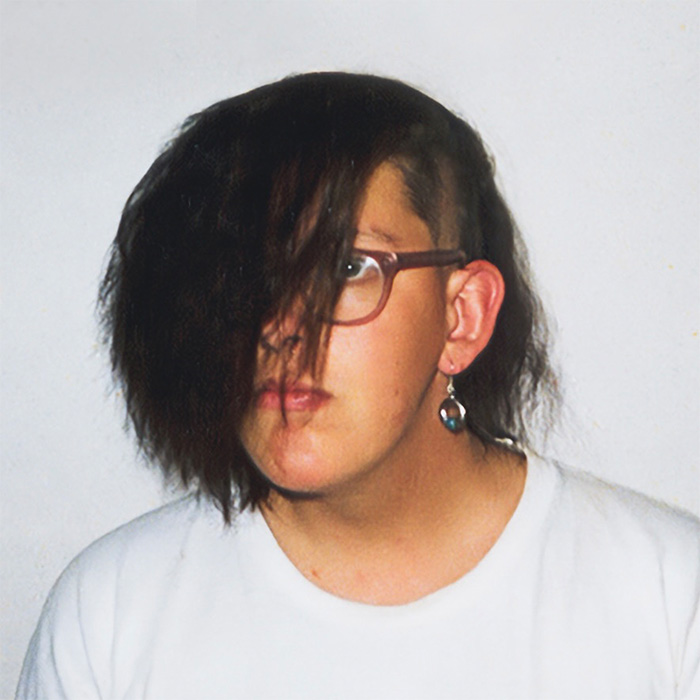 Jugendfoto von Franz Moped mit halblangem Seitenscheitel, Seitenschnitt, Ohrring und weißem T-Shirt vor hellem Hintergrund