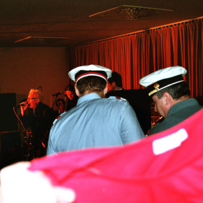 Zwei Polizisten von hinten, im Hintergrund Franz Moped auf der Bühne singend. Ein Polizeieinsatz während eines Konzertes der Band Houseverstand im Cinema Paradiso in St. Pölten 2005