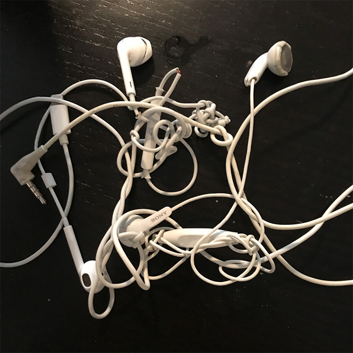 Extrem verknotete weiße Kabel-Kopfhörer auf dunkler Tischplatte