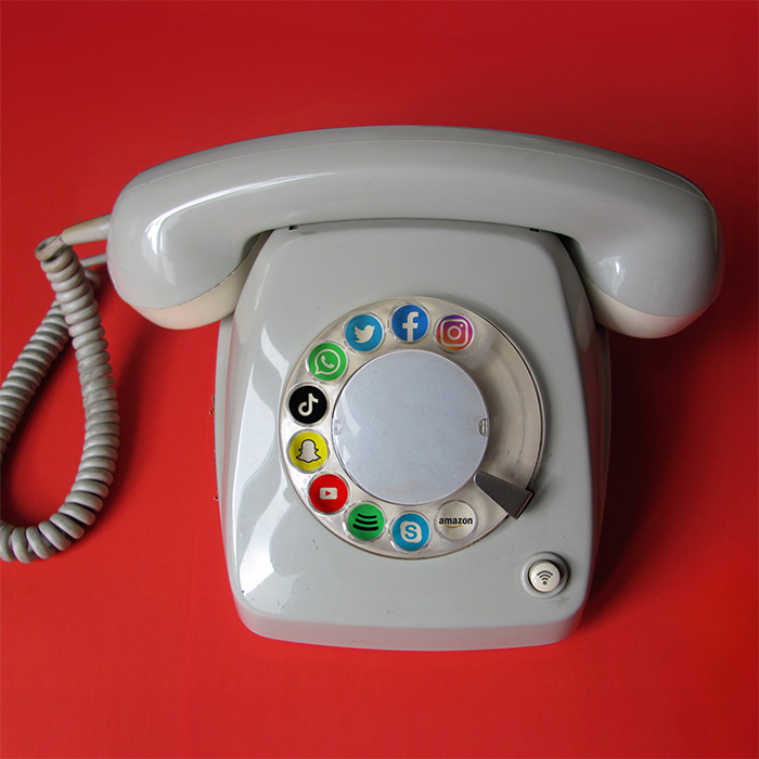 Graues Wählscheibentelefon vor rotem Hintergrund mit Logos von Social-Media-Plattformen anstelle von Ziffern auf der Wählscheibe